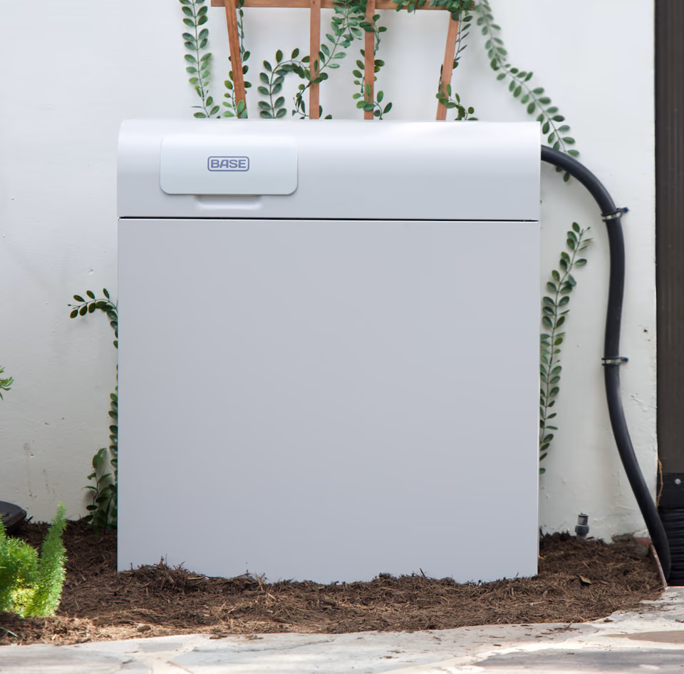 A Base Core home battery installed against a garden wall