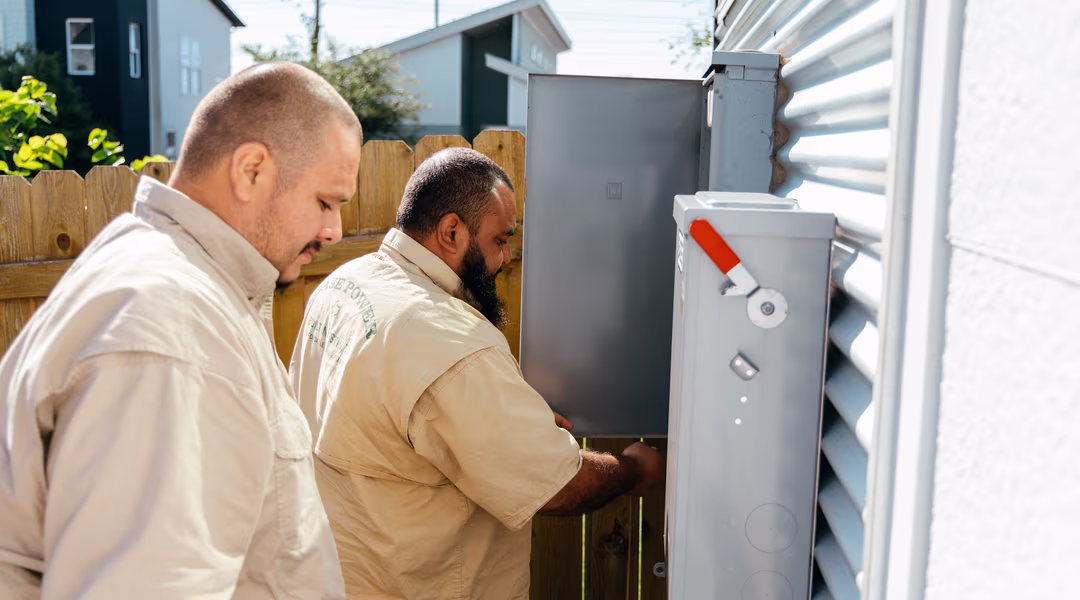 Two Base electricians wiring a home's meter panel during an install