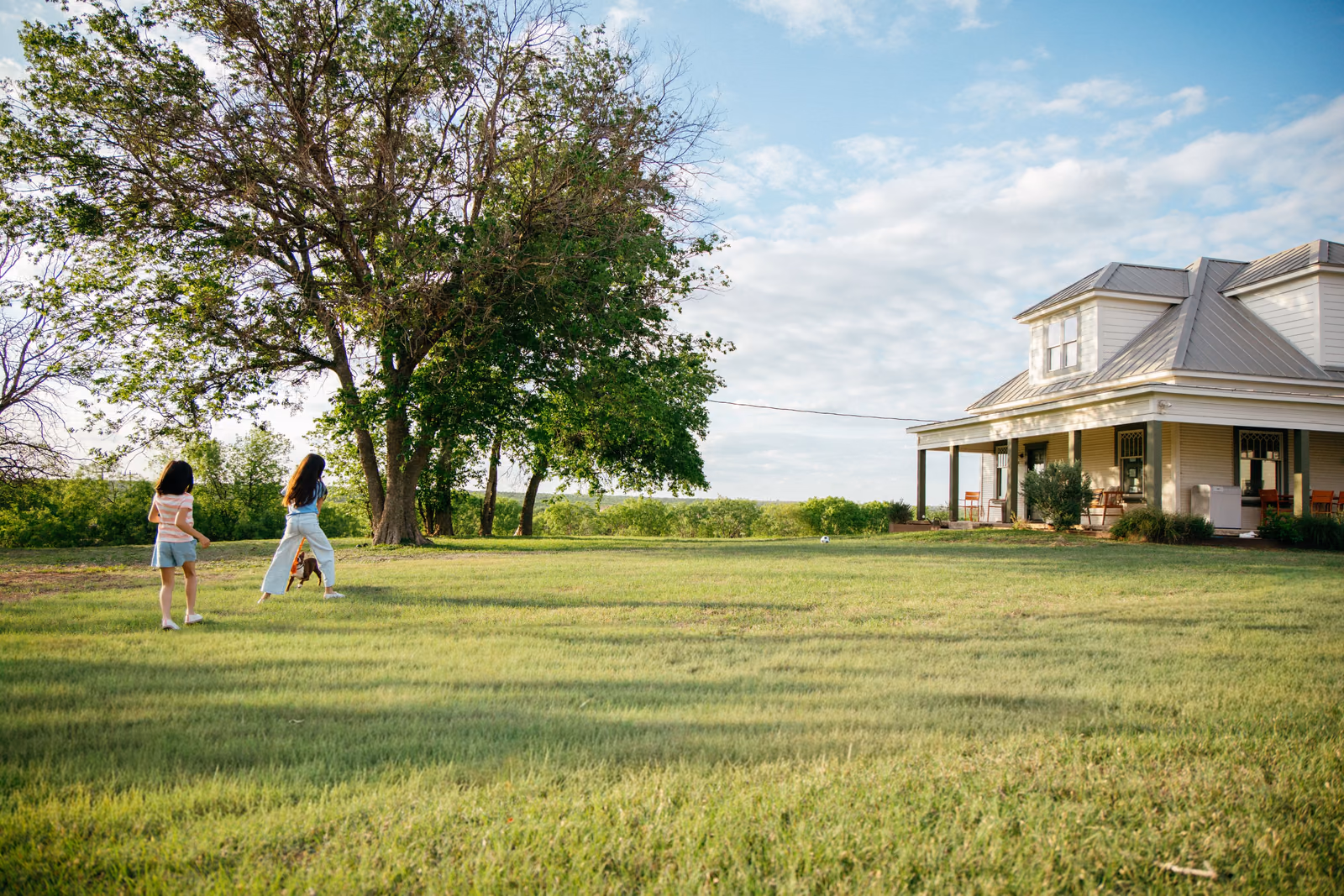 Two kids playing on the lawn in front of a Texas farmhouse