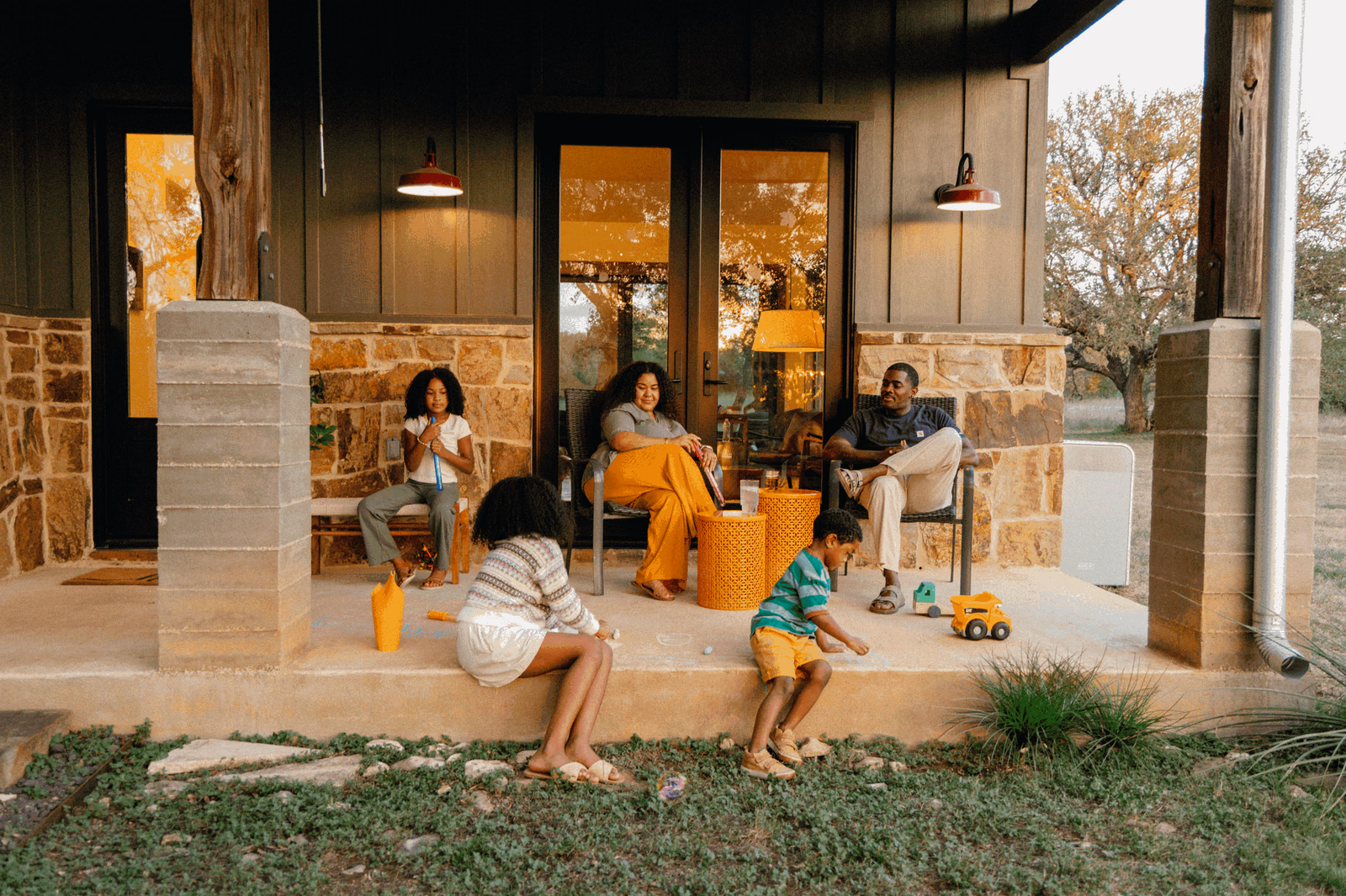 A family relaxing on their stone porch at dusk, with a Base Power battery beside the house