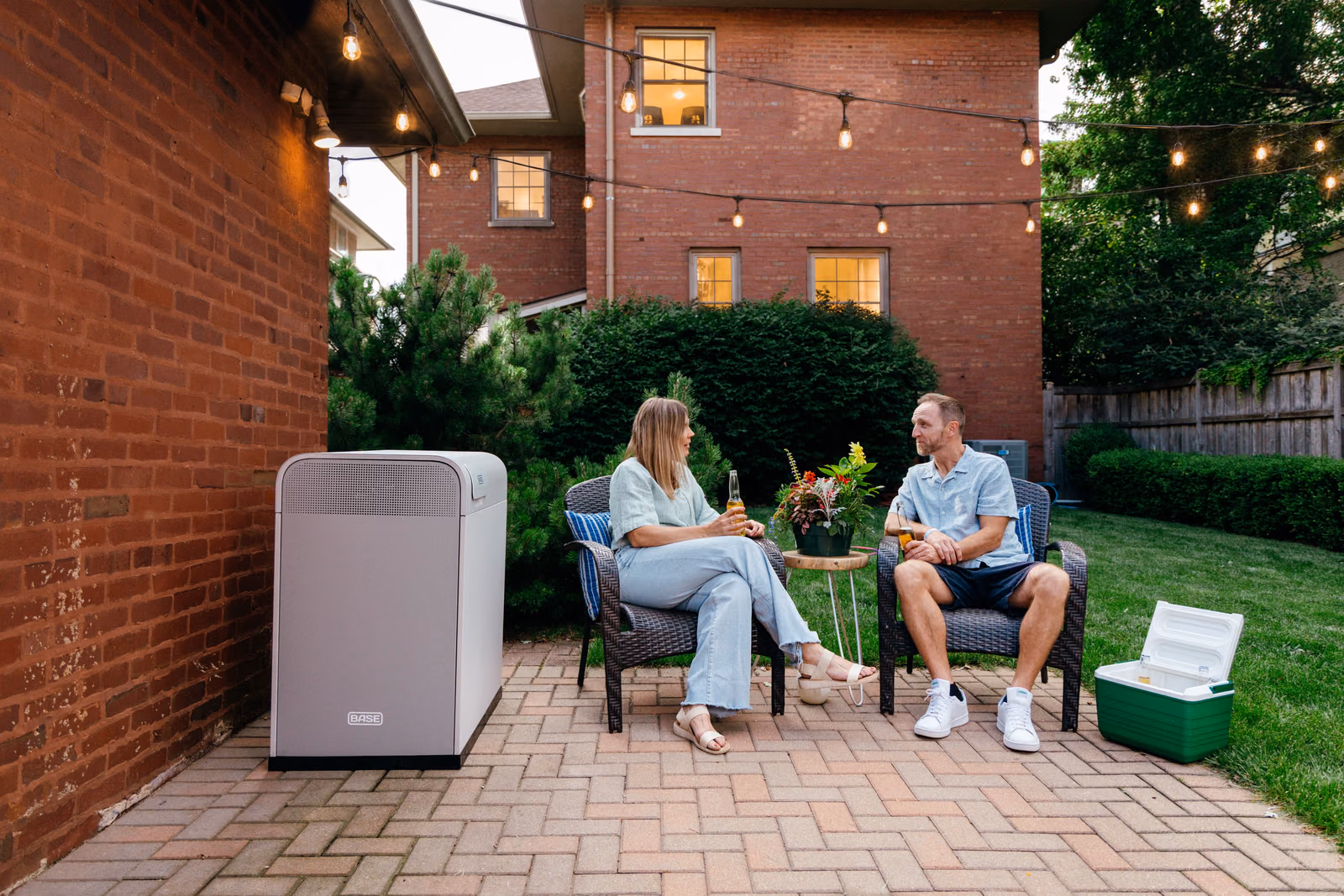 A couple relaxing on a patio at dusk beside a Base Power battery