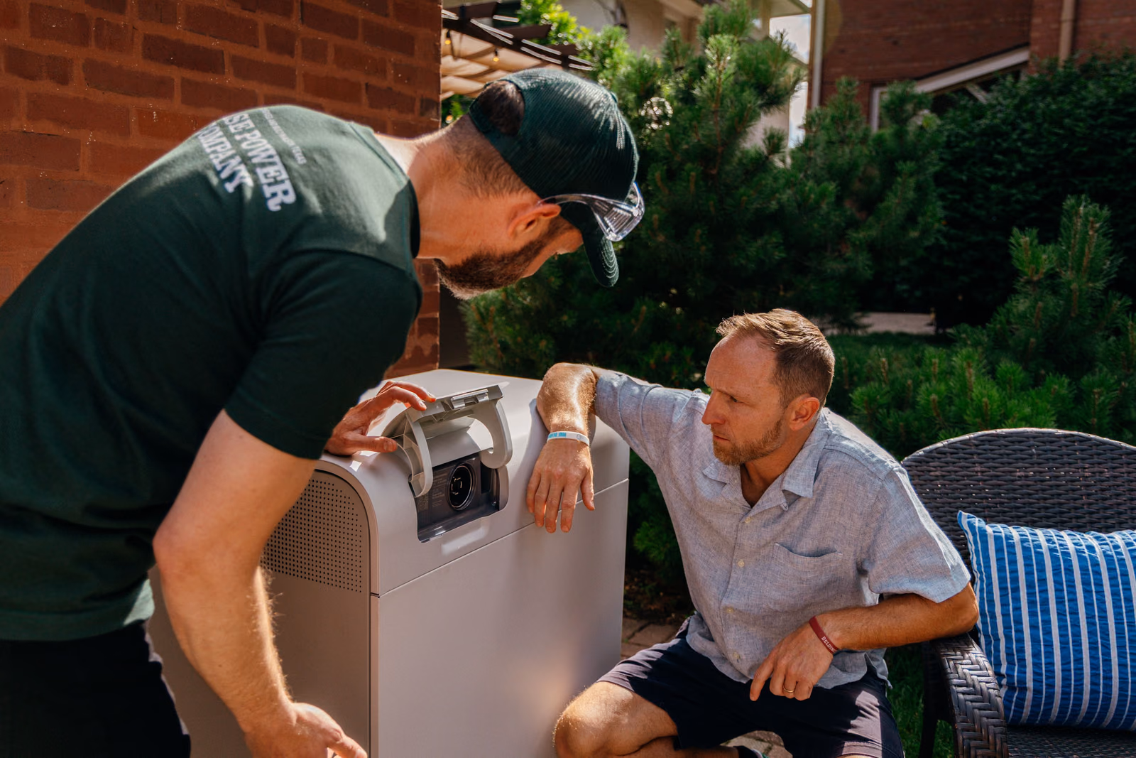 A Base Power technician and a homeowner beside a Base battery on a patio
