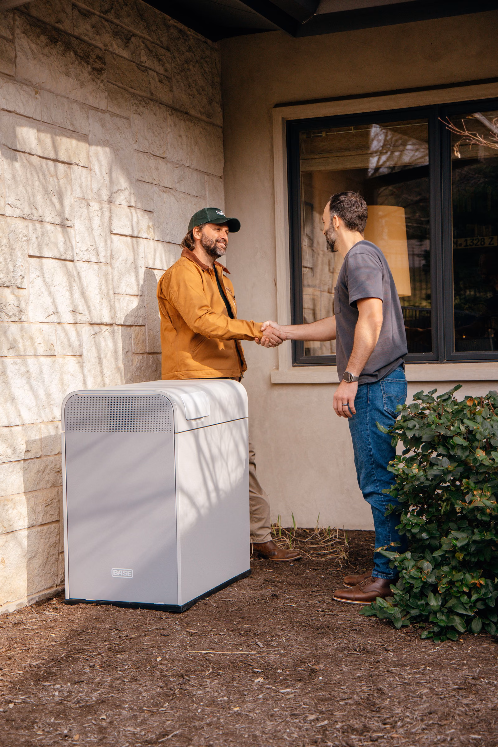 A Base Power installer shaking hands with a homeowner beside a Base battery