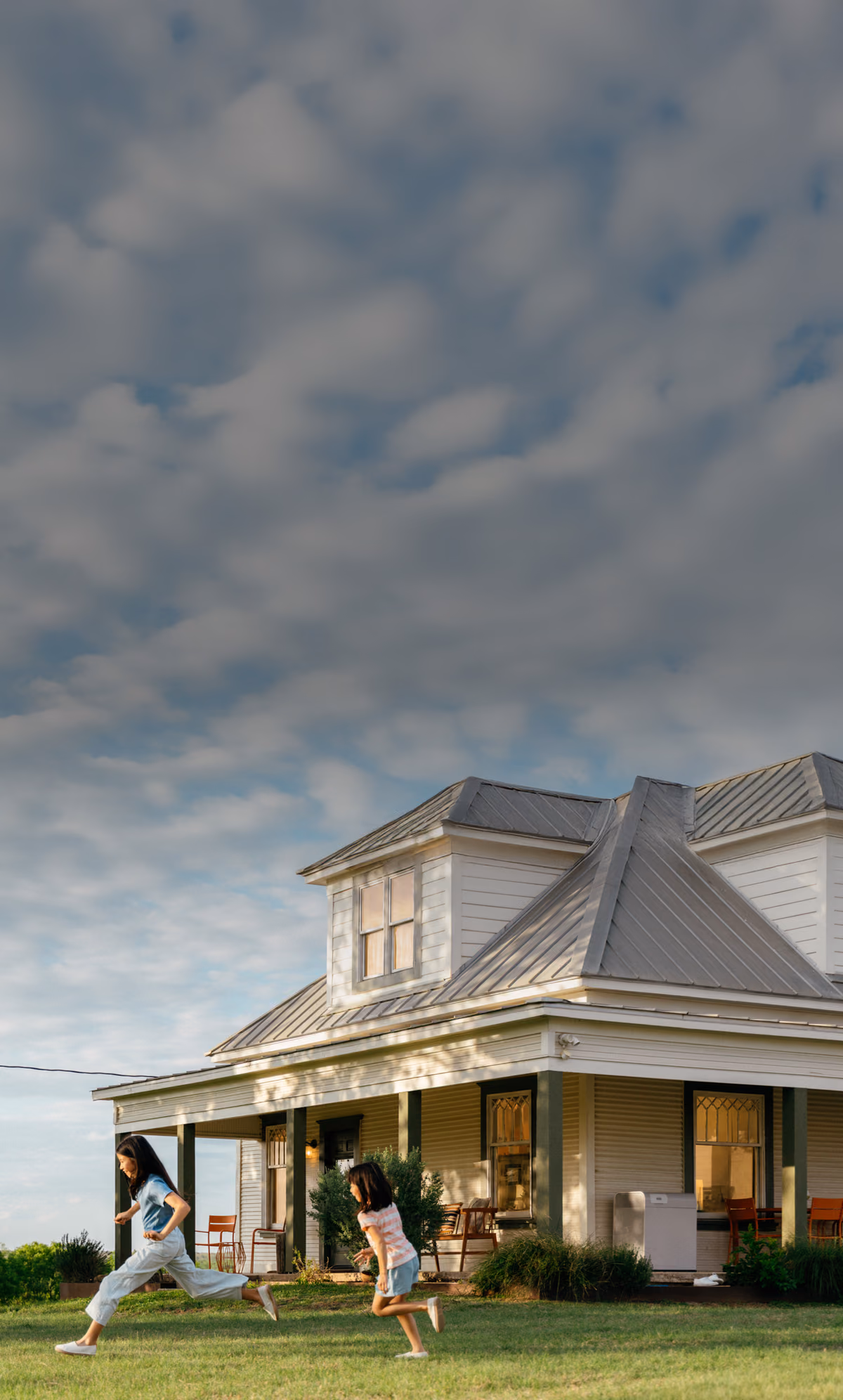 Two children playing on the lawn in front of a Texas farmhouse at dusk