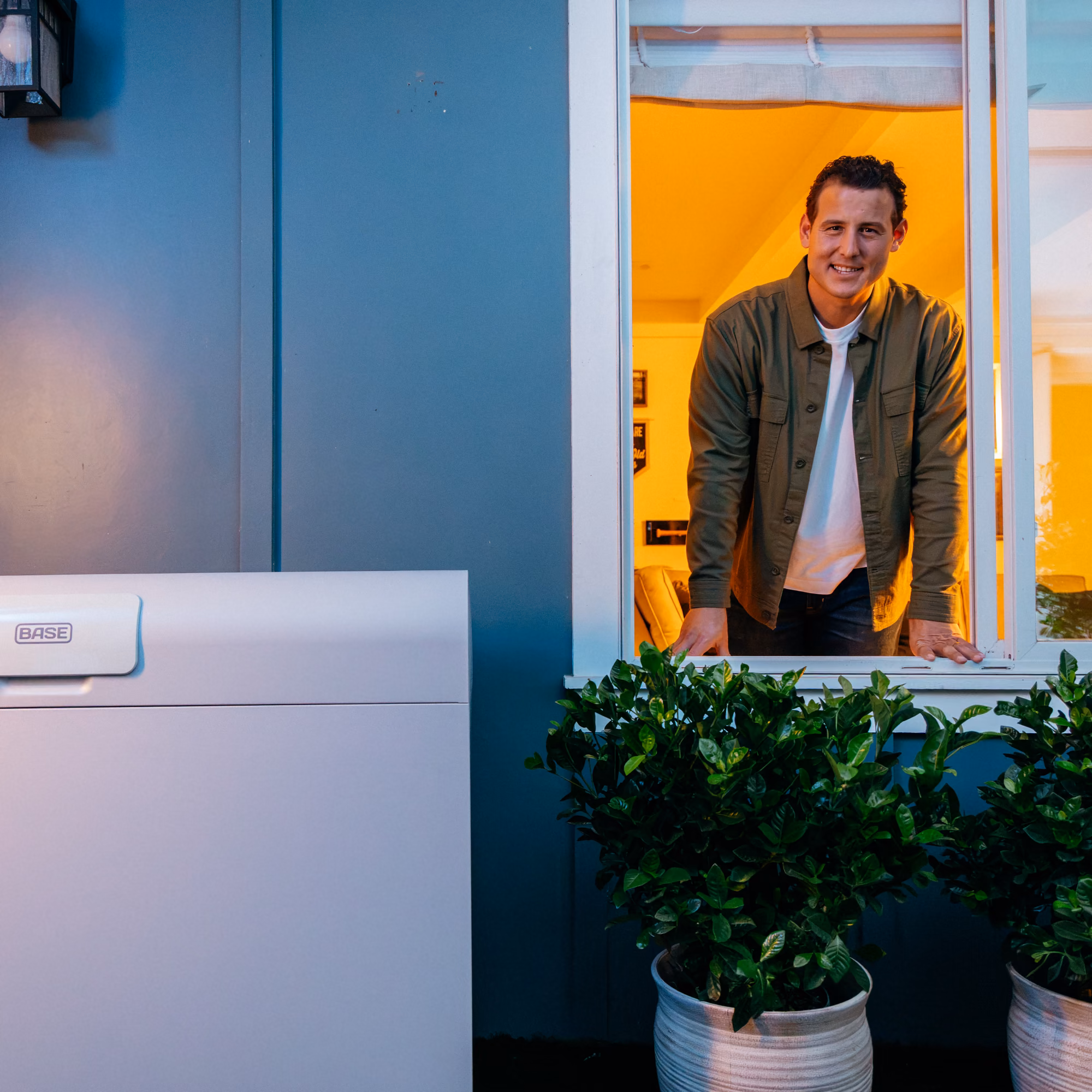 Anthony Rizzo leaning out of a lit window at dusk, a Base battery beside it