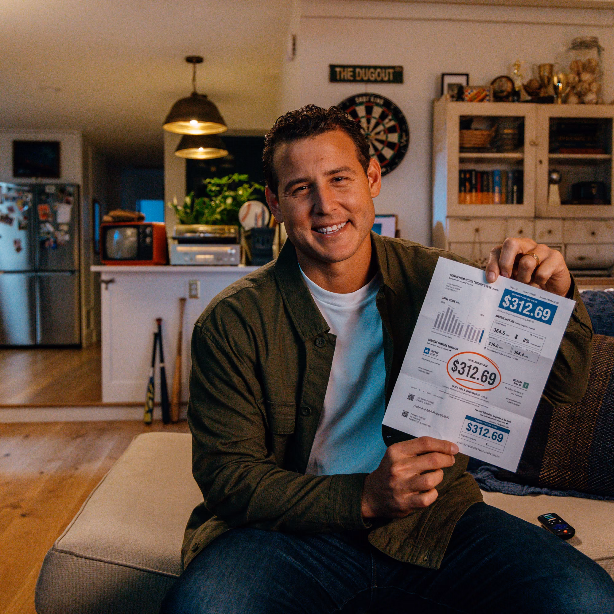 Anthony Rizzo on a couch at home, holding up an electricity bill