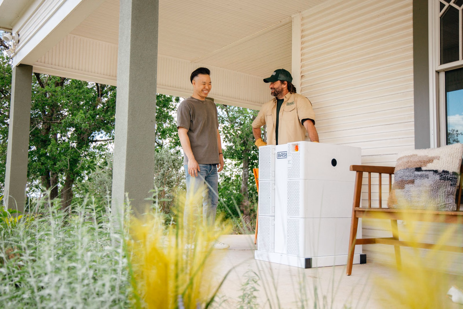 A Base Power technician and a homeowner beside a newly installed Base battery on a porch