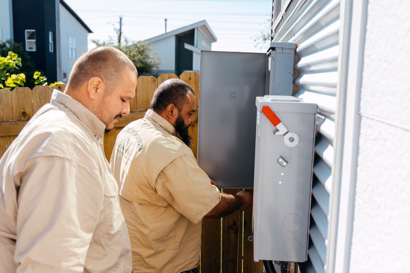 Electricians installing equipment beside a home's electric meter