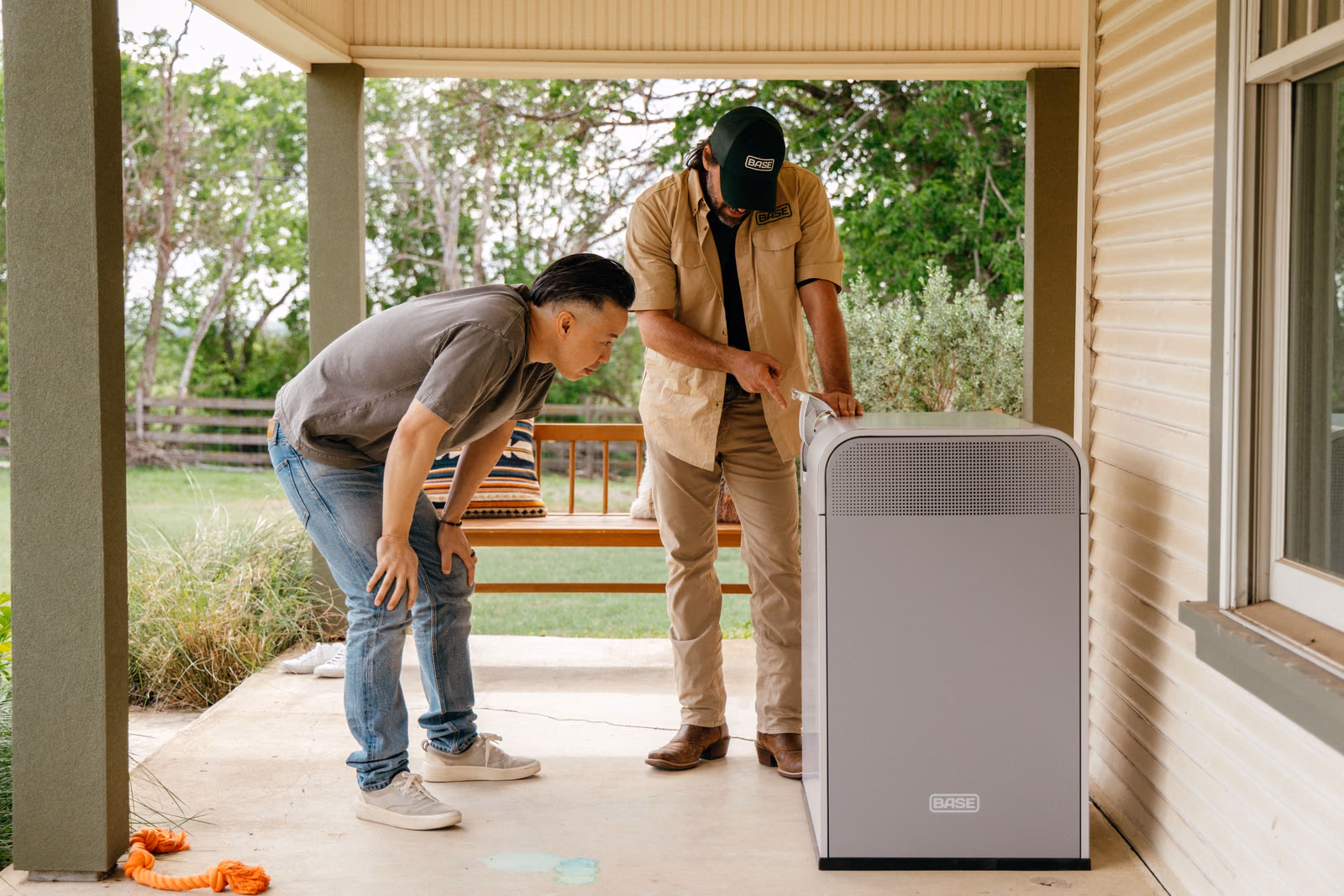 A homeowner and a Base Power technician beside a Base Power battery on a porch